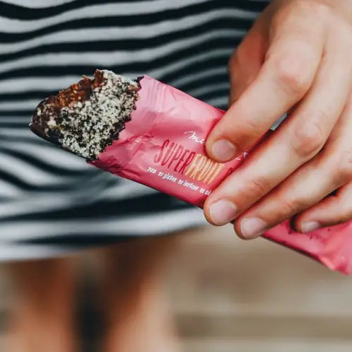 Áfonyás-meggyes Mendula szelet, rózsaszín csomagolásban. Éppen beleharaptak és látszik az áfonya és a meggy kontúrja.