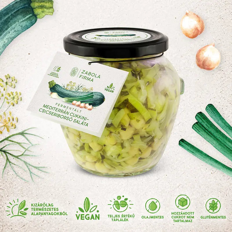 A kép közepén cukkini matricás üveget látsz, az üvegben a felszeletelt cukkinik és csicseriborsó úsznak, az üveg körül peidg cukkinik és csicseriborsók vannak.