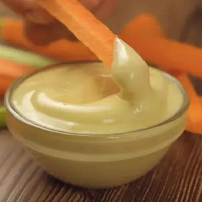 Pödör mézes-mustár látható a képen egy kis üvegtálkában, amint répahasábbal mernek ki egy falat mustárt.