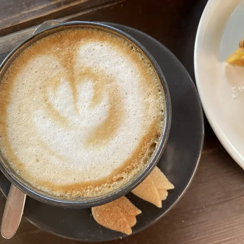 Felülről fotózva szívalakben elrendezett kávéhab és kávésbörgre látható, a fekete kávétányéron Sucrobello tulipán formacukor látható.