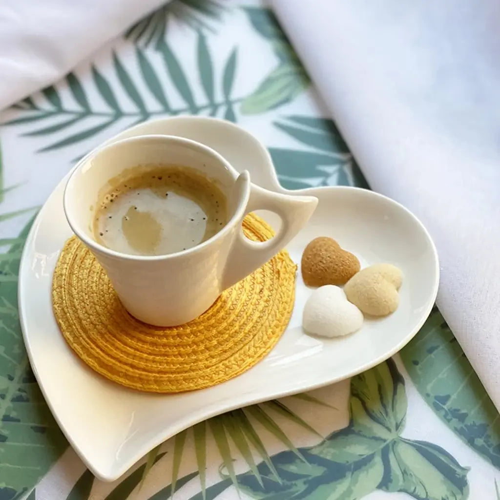 Reggeliző hangulat, egy porcelán kávéscsésze mellett, szívalakú tányéron a Suchrobbeló szívalakú formacukrai láthatóak. A terítőn zöld virágmintán láthatóak.