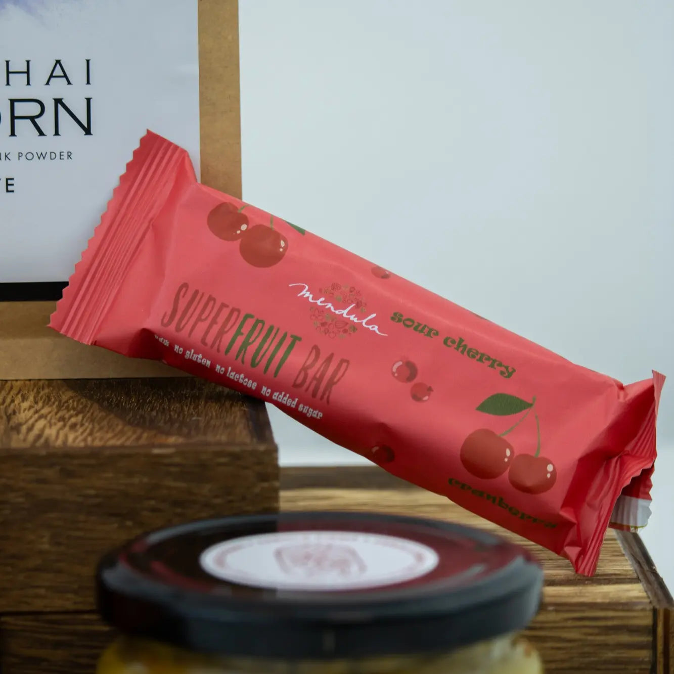 Mendula cseresznyés szelet, szép piros, cseresznyeszínű csomagolásban, egy barna dobozon. a kép eléterében egy fekete kupak van elmosódva. 