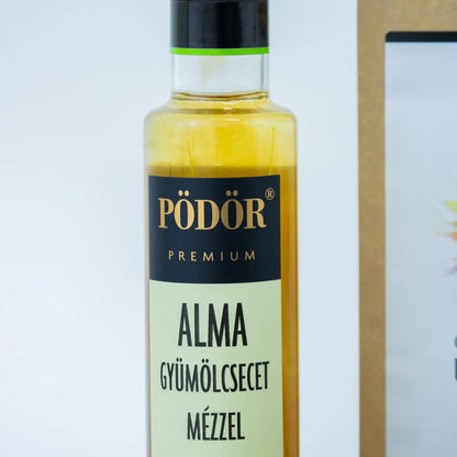 Pödör Alma gyümölcsecetről egy közeli képet láthasz. Az üvegben lévő ecet arany színű.