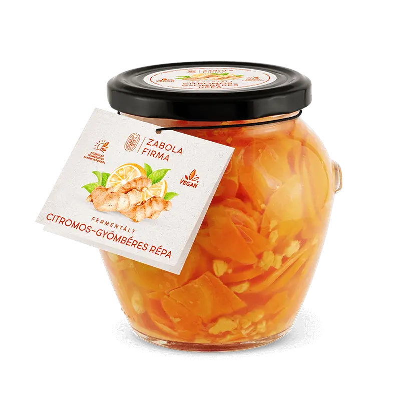 Az üvegbe ccitromos- gyömbéres répa van, látszanak a gyömbér darabkák és a szépen felvágott répaszeltek. Az üveg körül gyömbér, citrom és répa darabkák találhatóak. 