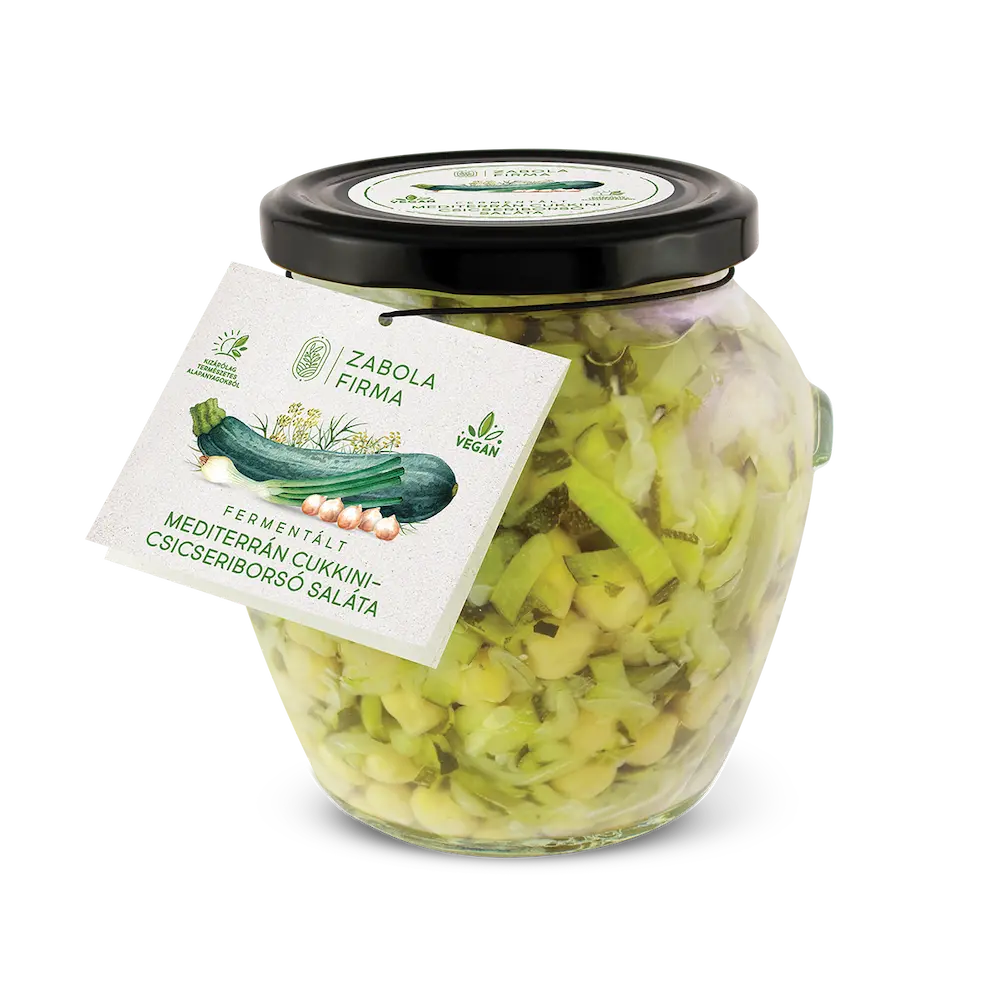 A kép közepén cukkini matricás üveget látsz, az üvegben a felszeletelt cukkinik és csicseriborsó úsznak, az üveg körül peidg cukkinik és csicseriborsók vannak. 