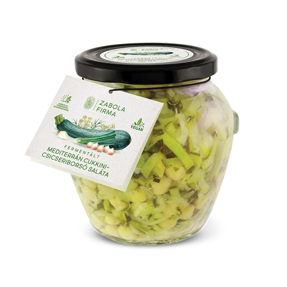 A kép közepén cukkini matricás üveget látsz, az üvegben a felszeletelt cukkinik és csicseriborsó úsznak, az üveg körül peidg cukkinik és csicseriborsók vannak. 