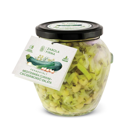 A kép közepén cukkini matricás üveget látsz, az üvegben a felszeletelt cukkinik és csicseriborsó úsznak, az üveg körül peidg cukkinik és csicseriborsók vannak. 