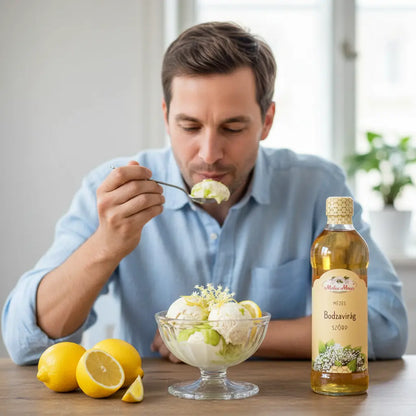 Egy kék inges férfi, bodzaszörppel ízesítette vanília fagylalot eszik üveg tálból, a tál mellett citromok vannak, fagylalt tetején bodzavirágok. 