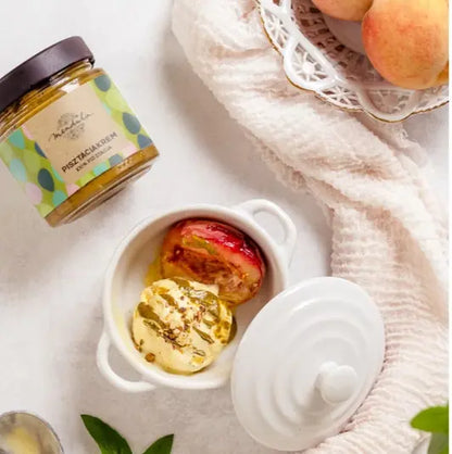 Mendula pisztáciakrémmel elkészített félbevágott barack és vaníliafagylalt látható egy porceláncsészében. A képen látható a Mendula pisztáciakrémes üvege is. 